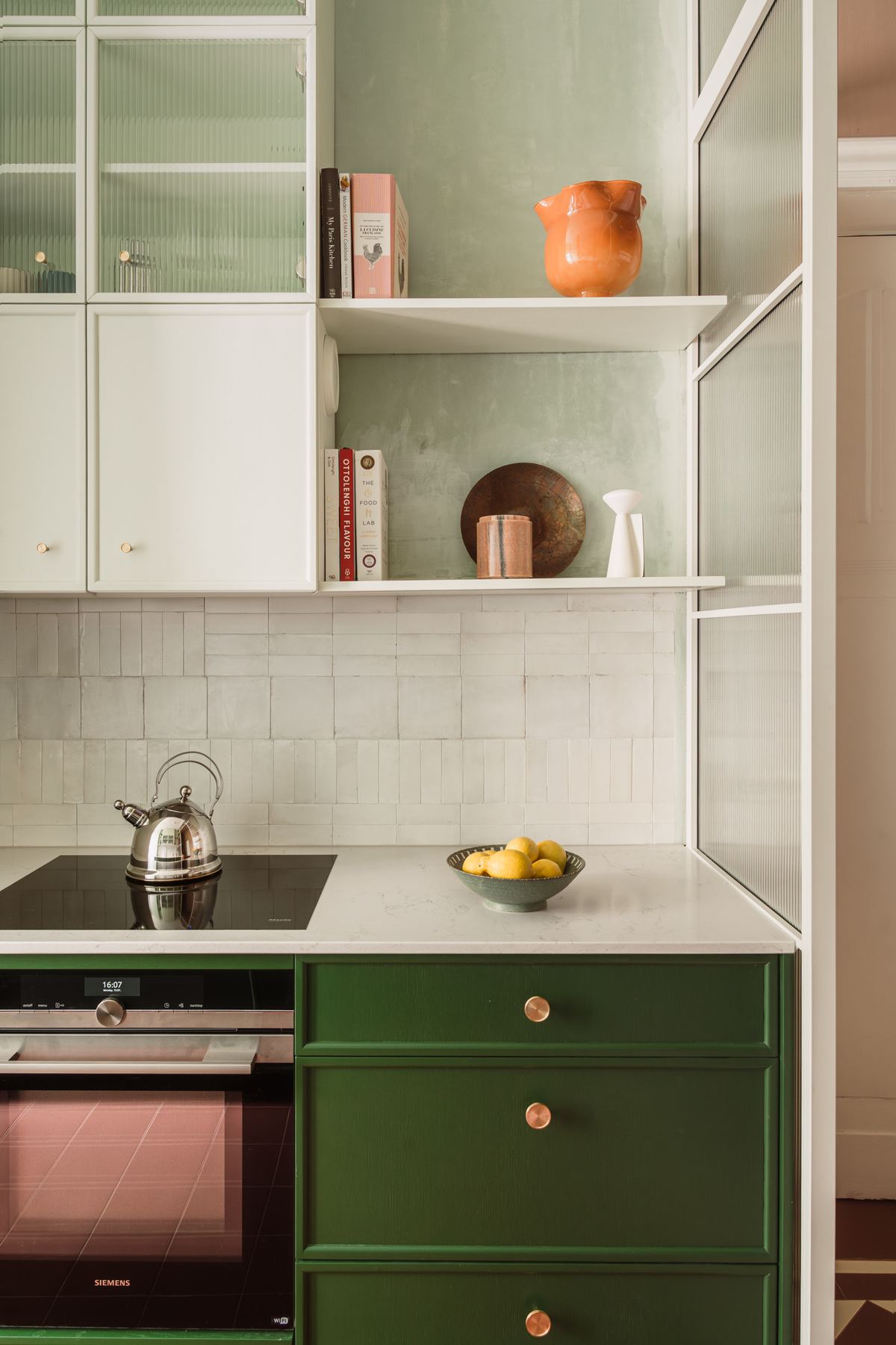 An induction stove set into the counter with an oven below it, a kettle on the hob and open shelving above.